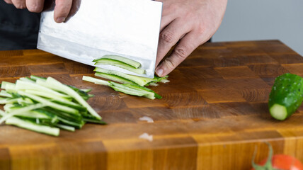 Close up of Chef cook hands chopping vegetables for traditional Asian cuisine with Japanese knife. Professional Sushi chef cutting cucumber for rolls.