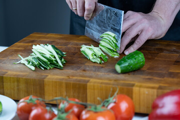 Close up of Chef cook hands chopping vegetables for traditional Asian cuisine with Japanese knife. Professional Sushi chef cutting cucumber for rolls.