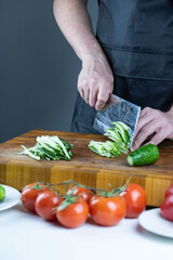 Close up of Chef cook hands chopping vegetables for traditional Asian cuisine with Japanese knife. Professional Sushi chef cutting cucumber for rolls.