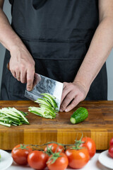 Close up of Chef cook hands chopping vegetables for traditional Asian cuisine with Japanese knife. Professional Sushi chef cutting cucumber for rolls.