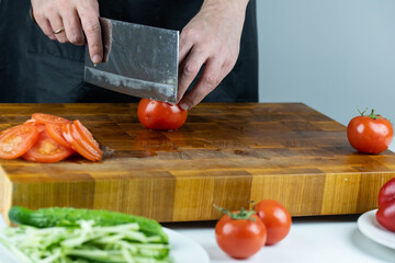 Close up of Chef cook hands chopping vegetables for traditional cuisine with Japanese knife. Professional chef cutting tomato on wooden board.