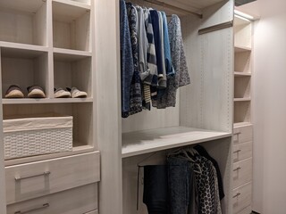 walk in closet with shirts and pants hanging up on hangers and shoes on the shelving