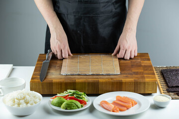 Closeup of chef hands preparing japanese food. Professional chef making sushi at restaurant. Man hands making traditional asian sushi rolls on cutting board.