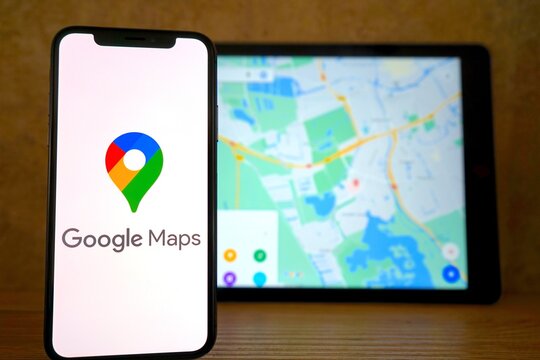 Google Maps Logo mit Schriftzug auf einem Smartphone angezeigt, im Hintergrund ein Tablet mit einer Kartenansicht von Google Maps