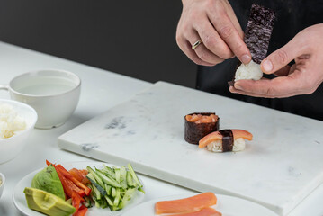 Closeup of chef hands preparing japanese food. Professional chef making sushi at restaurant. Man hands making traditional asian sushi rolls on cutting board.