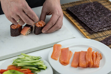 Closeup of chef hands preparing japanese food. Professional chef making sushi at restaurant. Man hands making traditional asian sushi rolls on cutting board.