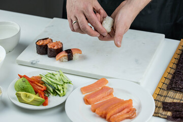 Closeup of chef hands preparing japanese food. Professional chef making sushi at restaurant. Man hands making traditional asian sushi rolls on cutting board.