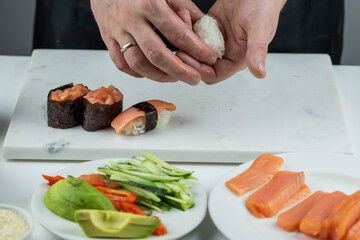Closeup of chef hands preparing japanese food. Professional chef making sushi at restaurant. Man hands making traditional asian sushi rolls on cutting board.