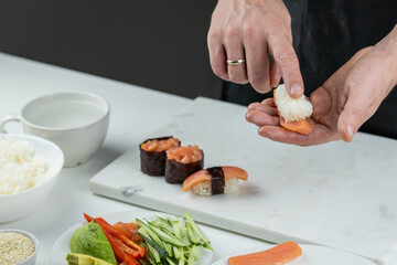 Closeup of chef hands preparing japanese food. Professional chef making sushi at restaurant. Man hands making traditional asian sushi rolls on cutting board.