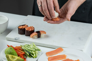 Closeup of chef hands preparing japanese food. Professional chef making sushi at restaurant. Man hands making traditional asian sushi rolls on cutting board.