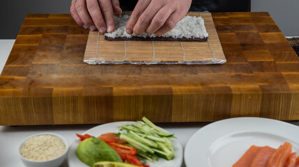 Closeup of chef hands preparing japanese food. Professional chef making sushi at restaurant. Man hands making traditional asian sushi rolls on cutting board.