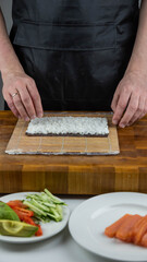 Closeup of chef hands preparing japanese food. Professional chef making sushi at restaurant. Man hands making traditional asian sushi rolls on cutting board.