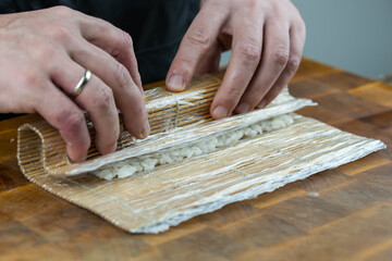 Closeup of chef hands preparing japanese food. Professional chef making sushi at restaurant. Man hands making traditional asian sushi rolls on cutting board.