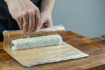 Closeup of chef hands preparing japanese food. Professional chef making sushi at restaurant. Man hands making traditional asian sushi rolls on cutting board.