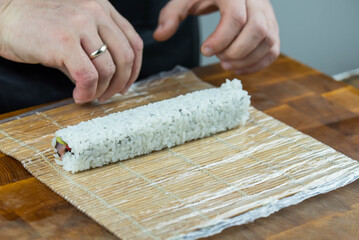 Closeup of chef hands preparing japanese food. Professional chef making sushi at restaurant. Man hands making traditional asian sushi rolls on cutting board.