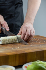 Closeup of chef hands preparing japanese food. Professional chef making sushi at restaurant. Man hands making traditional asian sushi rolls on cutting board.