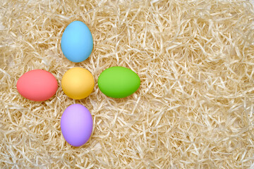 Fototapeta na wymiar Colored chicken eggs in the form of a flower on wood shavings. Rainbow colors. Easter. Shooting from above close up. Pattern. Place for text.
