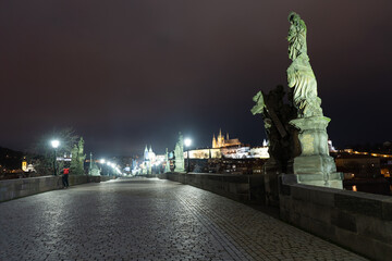 lit lanterns and illuminated statues and sidewalk with cobblestones on an empty charles bridge at...