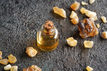 A bottle of frankincense essential oil with frankincense resin on a dark background