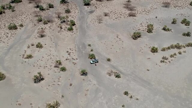 Looking down on a dry brown desert landscape with a off road vehicle in the middle of the shot camera moving away to very high veiwpoint Aerial Video