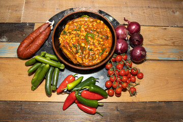 A bowl of delicious beans and sausages topped with garnish surrounded by the ingredients used to make the dish