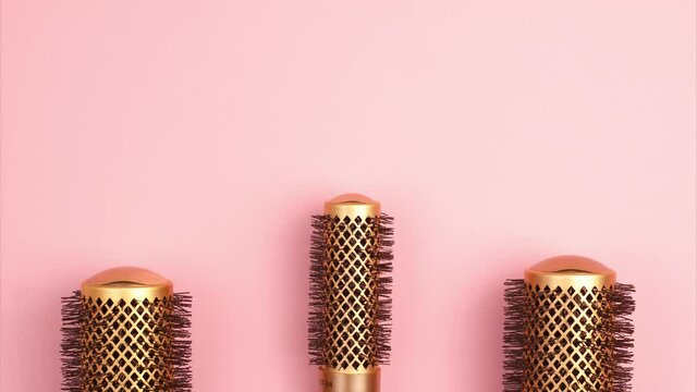 Stop motion animation of professional gold round hair brushes for styling at the bottom of the image template with copy space on pink background. Hairdresser salon equipment concept, premium set