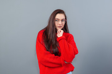 Fototapeta premium young emotional teenage female with glasses dressed in a red sweater posing on a gray background