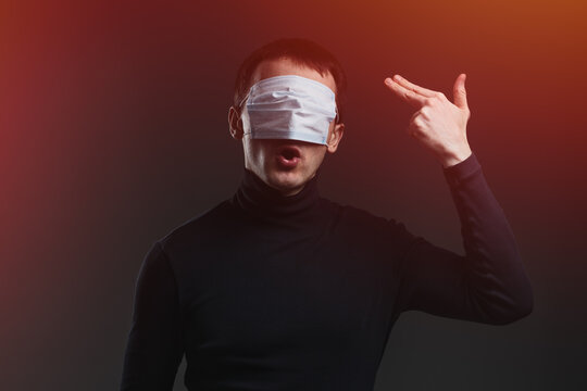 Young man with a blue face mask on his eyes showing gesture of shooting himself. Concept of anxiety and panic during global covid pandemic.