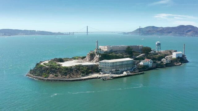 Aerial Alcatraz island with Golden Gate bridge on motion background. Historic prison building in green San Francisco bay area waters on summer day. World famous touristic landmarks and attraction 4K