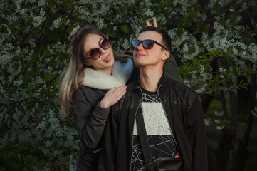 A couple in love, a girl and a guy together on the street in the spring against a background of greenery and flowers in jackets and jeans and in sunglasses