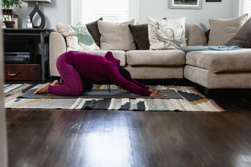 Black woman doing childs pose at home in living room, yoga flow
