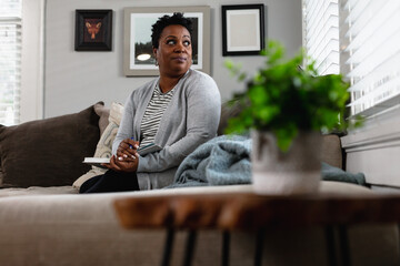 Black woman focused and thinking on couch at home, planning and paying bills