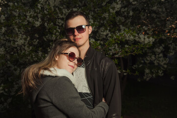 A couple in love, a girl and a guy together on the street in the spring against a background of greenery and flowers in jackets and jeans and in sunglasses