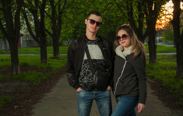 A couple in love, a girl and a guy together on the street in the spring against a background of greenery and flowers in jackets and jeans and in sunglasses