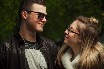 A couple in love, a girl and a guy together on the street in the spring against a background of greenery and flowers in jackets and jeans and in sunglasses
