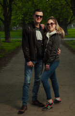 A couple in love, a girl and a guy together on the street in the spring against a background of greenery and flowers in jackets and jeans and in sunglasses