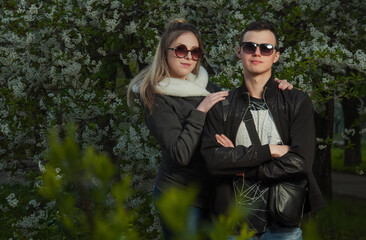 A couple in love, a girl and a guy together on the street in the spring against a background of greenery and flowers in jackets and jeans and in sunglasses