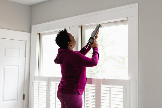 Black woman caulks window sill, energy efficiency, home improvement, DIY