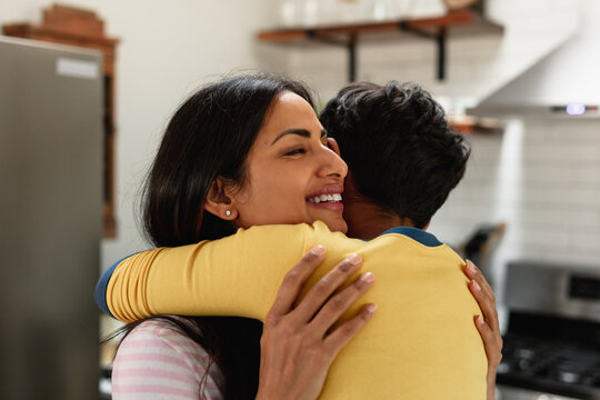 Smiling Indian Mom Embracing Son At Home In Kitchen