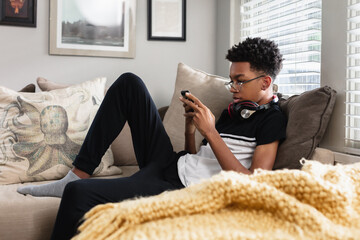 Teen boy on phone at home on couch, African American, cozy