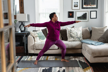 Black woman does warrior yoga pose, at home fitness and wellness