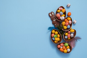 Flat lay Easter eggs hunt concept with chocolate eggs and bunny on blue background. View from above