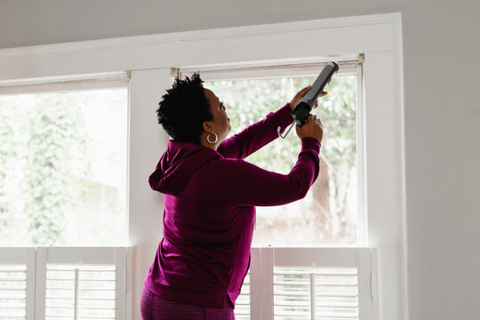 Black woman caulks window sill, energy efficiency, home improvement, DIY