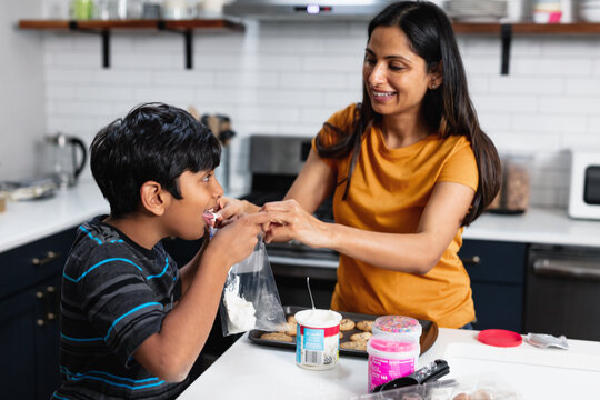 Indian boy tastes frosting while putting icing on fresh baked cookies