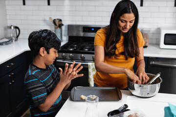 Indian mother and son preparing homemade treats in kitchen