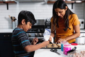 Indian mother and son decorating fresh baked cookies in the kitchen