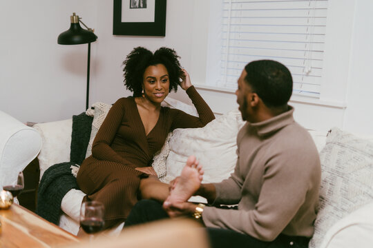 Man Helps Girlfriend Take Off Shoes To Relax On Couch At Home