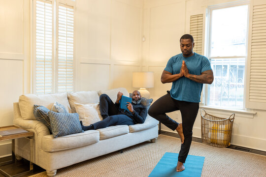 Man watches his partner doing yoga, tree pose