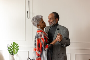 Black senior couple slow dancing at home in living room, formal wear, anniversary