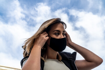Short-haired blonde woman putting on a black mask to avoid catching corona virus
